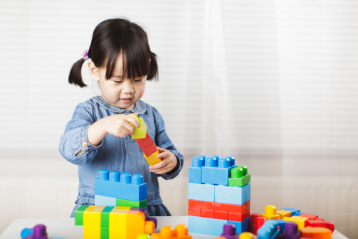 Young girl playing with plastic stack blocks on a table.