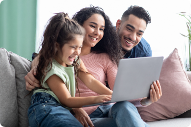 Happy family of young girl with lady and man sitting on couch focussing on laptop.