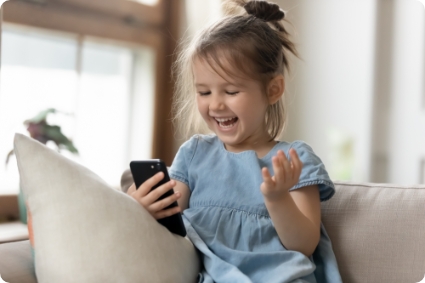 Happy young girl sitting on couch looking excitedly at a smart phone.
