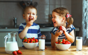Young boy and young girl happily eating bowls of strawberries with a healthy glass of milk